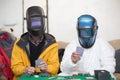 Two welders in welding masks play poker.