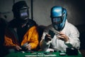 Two welders in welding masks play poker.