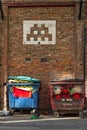 Two wheelie bins under a tiled mosaic Space Invader. Street art. Northern quarter. Manchester, England.