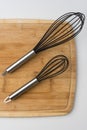 Two Whisks Angled on Wooden Cutting Board on White Background Royalty Free Stock Photo