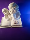 Two white angels and a book on a purple background figurine Royalty Free Stock Photo
