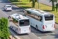 Two white buses, a large and a small one, travel opposite each other along the lanes, overtaking cars, aerial top view