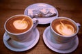 Two white ceramic cappuccino cups and cherry pie on a white ceramic plate with a wooden table in the background Royalty Free Stock Photo