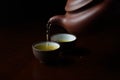 A green tea being poured into two cups on a dark background