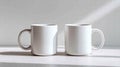Two white ceramic mugs sit side-by-side on a white surface, bathed in soft light. Royalty Free Stock Photo