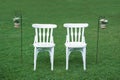 Two white chairs waiting for the grooms next to some floral decoration on the green grass. Royalty Free Stock Photo