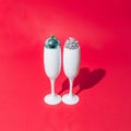 Two white champagne glasses with pine cone and light blue disco ball inside of them. Red pastel background. Minimal design Royalty Free Stock Photo