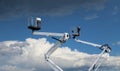 Two white cherry pickers against blue sky with clouds, Under there are fluffy clouds, above dark clouds Royalty Free Stock Photo