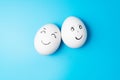 Two white chicken eggs with smiling faces on blue background Royalty Free Stock Photo