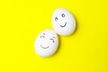 Two white chicken eggs with smiling faces on yellow background Royalty Free Stock Photo