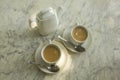 Two white cups with milk tea, spoons and a ceramic teapot on the marble surface of the table close-up Royalty Free Stock Photo