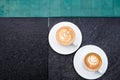 Two white cups of tasty cappucino with art latte on the edge of swimming pool