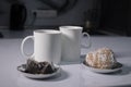 Two white cups of tea next to used tea bags next to gingerbread cookies on a white table in a gray kitchen