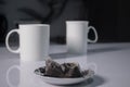 Two white cups of tea next to used tea bags on white table in gray kitchen