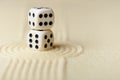 Two white dice with black dots on sand