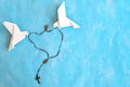 Two white dove origami carrying rosary or scapular in sky blue background.