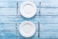 Two white empty plates and cutlery on blue table.