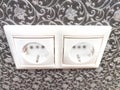 Two white European power outlets mounted on ornate wall. European Dual Socket on a Patterned Wall