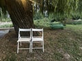 Two white folding chairs under a large tree in a peaceful park setting Royalty Free Stock Photo