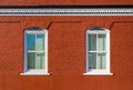 Two white framed windows in a red brick building with scrollwork and cornice