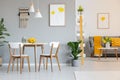 Two white lamps above a round dining table in open space apartment interior with yellow blanket on gray sofa. Real photo Royalty Free Stock Photo