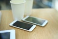 Two white mobile phones with tablet on wooden table background, blank screen electronic device with copy space. Royalty Free Stock Photo