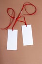 Two white paper tag with red ribbon and a bead on the brown background Royalty Free Stock Photo