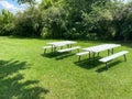 Two white picnic tables in a lush green garden area with grass lawn and woodland trees Royalty Free Stock Photo