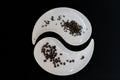 Two white plates with black coffee beans and dried leaves of green tea on black background Royalty Free Stock Photo