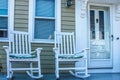 Two white rocking chairs with cushions  on porch outside neat frame house Royalty Free Stock Photo