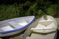 Two white row boats or dinghies on the sandy beach with wild plants and metal fence