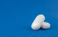 Two white tablets close-up on a blue background. Medicine