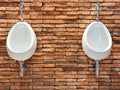 two white urinal for male decoration on oramge bricks wall . public install urine flush