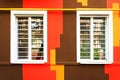 Two white windows on the background of a colored wall. The colored wall of the house is painted yellow, brown, orange Royalty Free Stock Photo