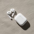 Two white wireless earbuds with silicone tips and a matching charging case are placed on a textured Royalty Free Stock Photo