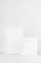 Two white wood blank rectangle and square photo frames on soft light table, plaster wall in modern minimal simple style. Royalty Free Stock Photo