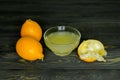 Two whole lemons, squeezed lemon and lemon juice in a glass cup, shot on a rough wooden background Royalty Free Stock Photo