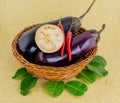 Two whole mature eggplants with capsicum in a wicker brown basket on a yellow background