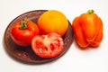 Two whole tomatoes on a clay plate and one half.Orange pepper is next to the plate. Royalty Free Stock Photo