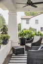 Two wicker chairs and pots of plants on the front porch of a historic craftsman house with blurred neighboring luxury home in back Royalty Free Stock Photo