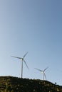 Two wind turbines spinning on a hilltop in a wind farm under a clear blue sky Royalty Free Stock Photo