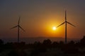 Two windmills facing the sun at sunset