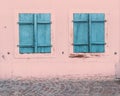 Two windows with closed blue wooden shutters on a old house with a pink wall Royalty Free Stock Photo