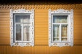 Two windows framed with white carved wooden jambs on the facade of a yellow painted Russian isba Royalty Free Stock Photo