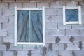 two windows on the side wall of an old concrete house with plastic covering them, which is covered in gray bricks Royalty Free Stock Photo