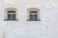 Two windows in thick brick mediewal wall under worn layer of white plaster