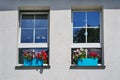 Two windows on a white wall in hot summer with blue flower boxes. Royalty Free Stock Photo