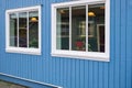 Two windows with white wood frames in a blue color wooden wall. Exterior of a wooden house with windows Royalty Free Stock Photo