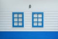 Two windows on white wood wall, outdoor view. Colorful blue window from front outside of house Royalty Free Stock Photo