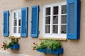 Two windows with white wooden frames, blue shutters and decorative flower boxes. Image of trendy decor, comfort, beautification Royalty Free Stock Photo
